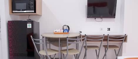 A compact room with a kitchenette, a flat-screen TV, a foldable dining table, and four chairs.