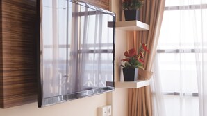 Een moderne woonkamer met een flatscreen televisie bevestigd aan een houten paneel, een witte console tafel met een afstandsbediening en een potplant op een zwevend schap.