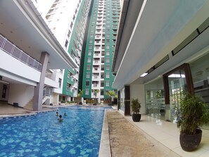 An indoor swimming pool with a view of high-rise buildings, potted plants, and a glass-walled area.