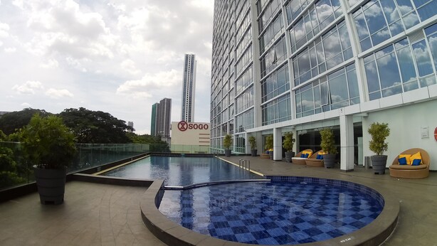 Um edifício moderno com uma grande fachada de vidro, um letreiro com 'Sogo' e uma área de piscina com espreguiçadeiras.