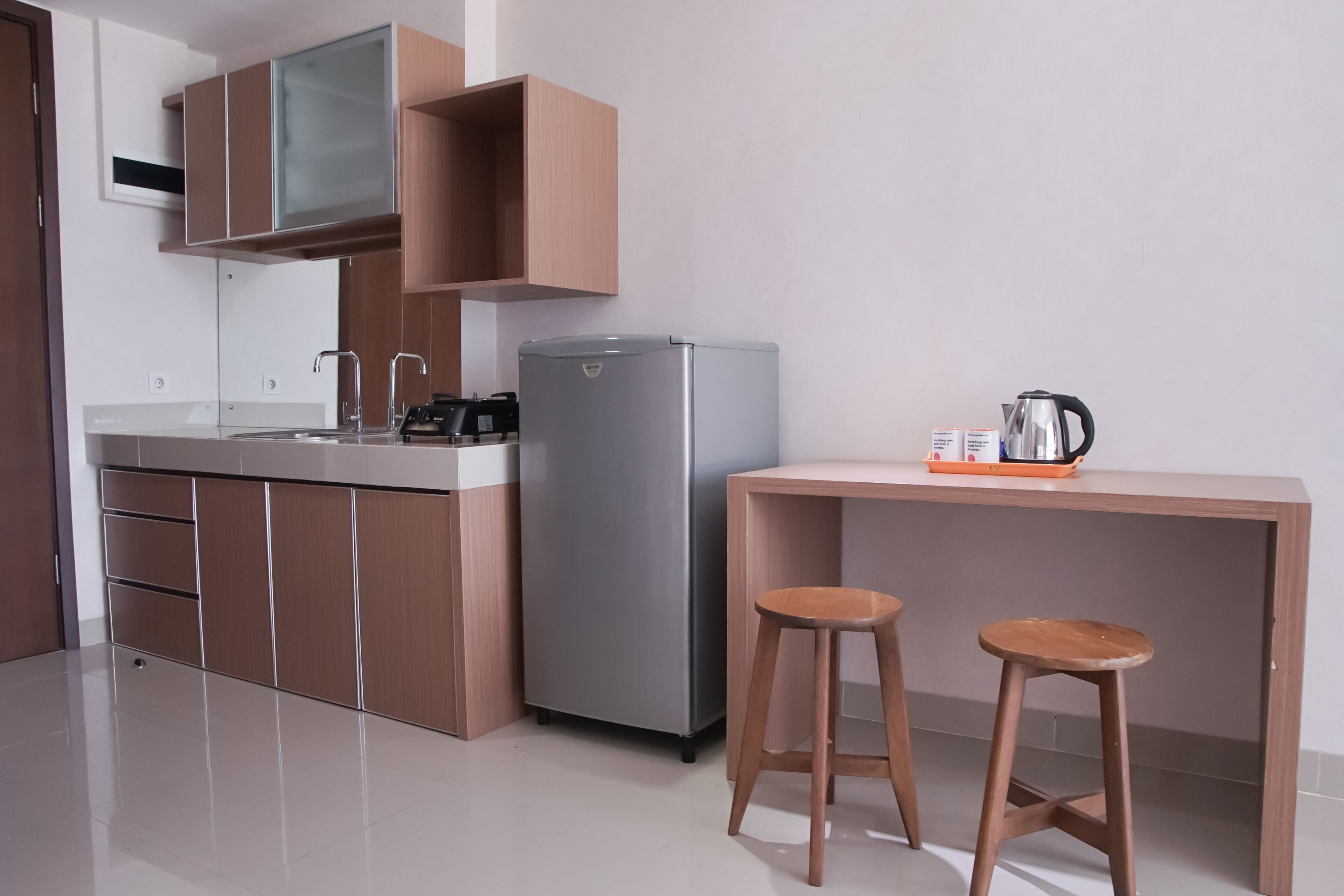 A compact kitchen with a refrigerator, a coffee maker, and two stools.