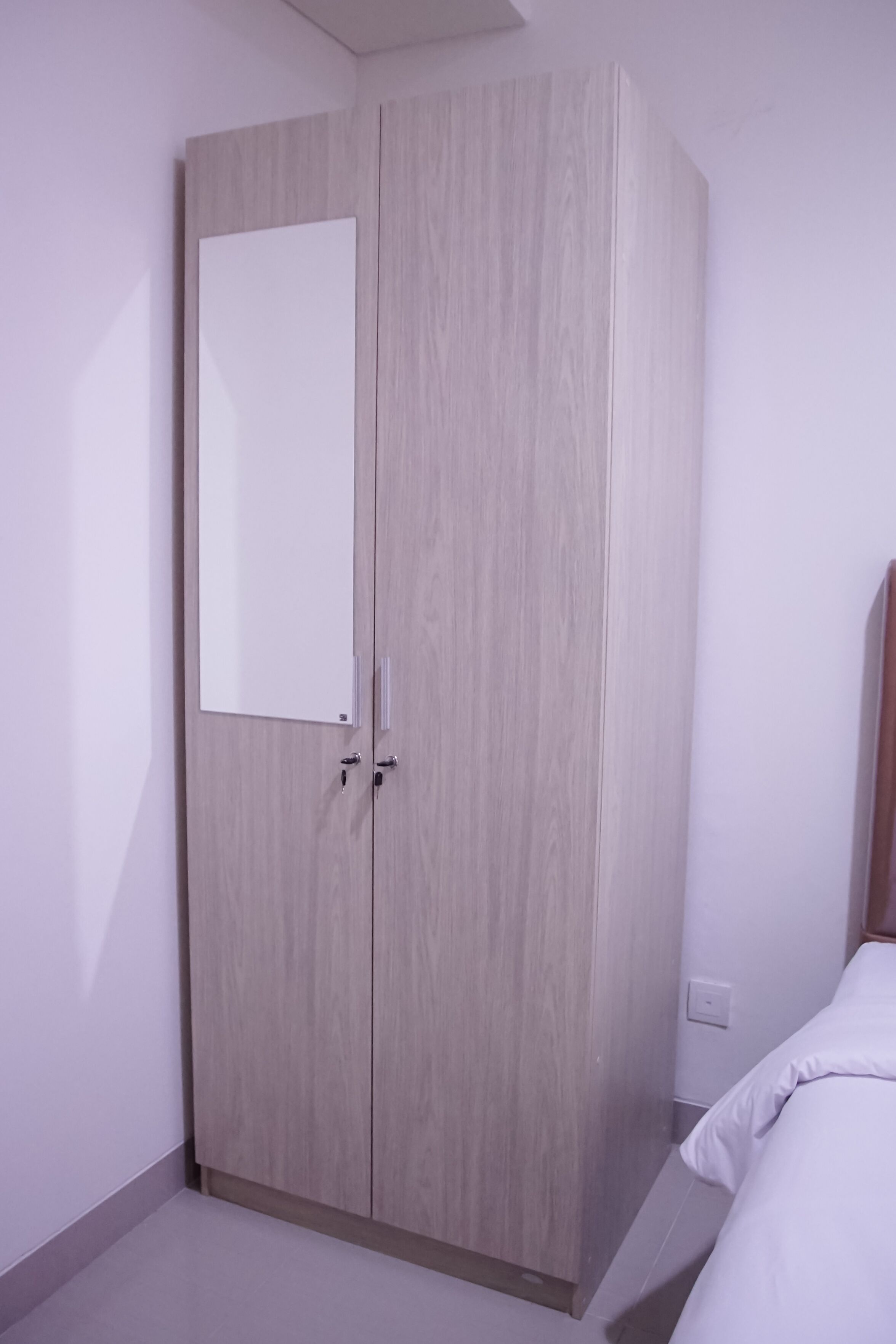 A room with a wardrobe, a bed, and a light switch on the wall.