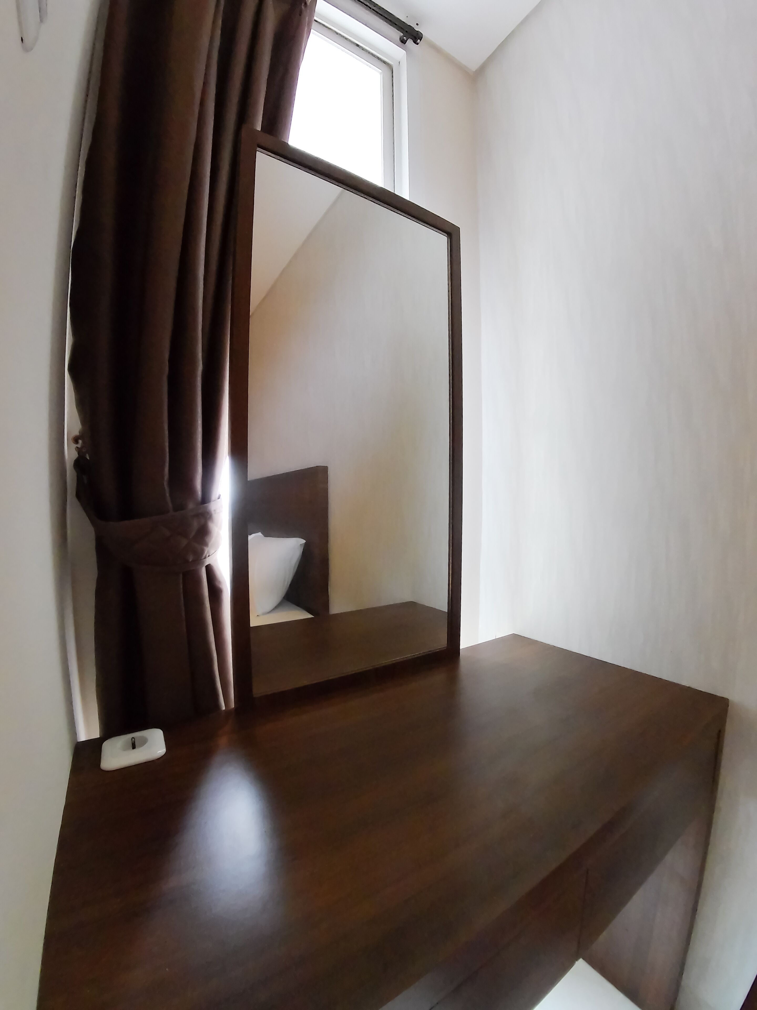 Un bureau en bois avec un miroir, un coussin blanc et une fenêtre avec des rideaux.