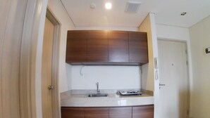 A small kitchen with a sink, a stove, and wooden cabinets. - Apatel Elpis Residences 09B01 (Jakarta)