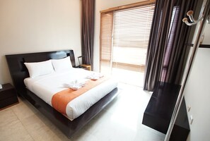 Cama bem arrumada com roupa de cama branca e laranja, mesa de cabeceira de madeira, cabeceira preta e uma janela com persianas.