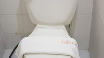 Un inodoro con tapa blanca, un rollo de papel higiénico y una bolsa naranja encima.