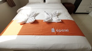 En snyggt bäddad säng med vita och orange sängkläder, två dekorativa rosetter och en logotyp på det orange överkastet.