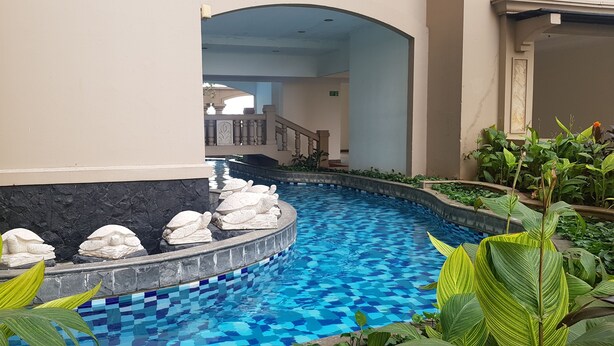 En pool med ett mosaikmönster, omgiven av grönska och stenskulpturer.