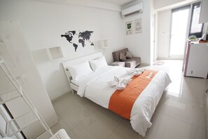 A hotel room with a bed, a world map on the wall, a chair, and a desk with a computer. - Apatel The OAK Tower Pulo Gadung (Jakarta)