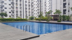 A swimming pool with a wooden deck, surrounded by greenery and a small pavilion. - Apatel The OAK Tower Pulo Gadung (Jakarta)