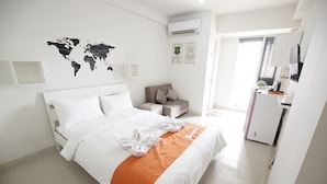 A neatly made bed with an orange accent, a world map on the wall, a small seating area, and a kitchenette. - Apatel The OAK Tower Pulo Gadung (Jakarta)