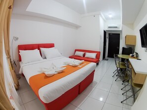 A hotel room with a large bed, a red sofa, a small table with chairs, and a TV.