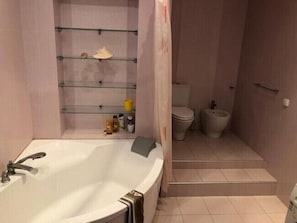 A bathroom with a bathtub, toilet, bidet, and shelves with toiletries. - Apart Kiev Chernovola 2 (Kyiv)