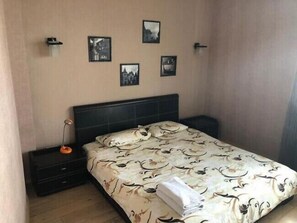 A bedroom with a bed, a nightstand, and a wall-mounted shelf with pictures. - Apart Kiev Chernovola 2 (Kyiv)