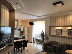A modern living room with a flat-screen TV, a dining area with a table and chairs, and a kitchen with a refrigerator and microwave. - Apart Kiev Chernovola 2 (Kyiv)