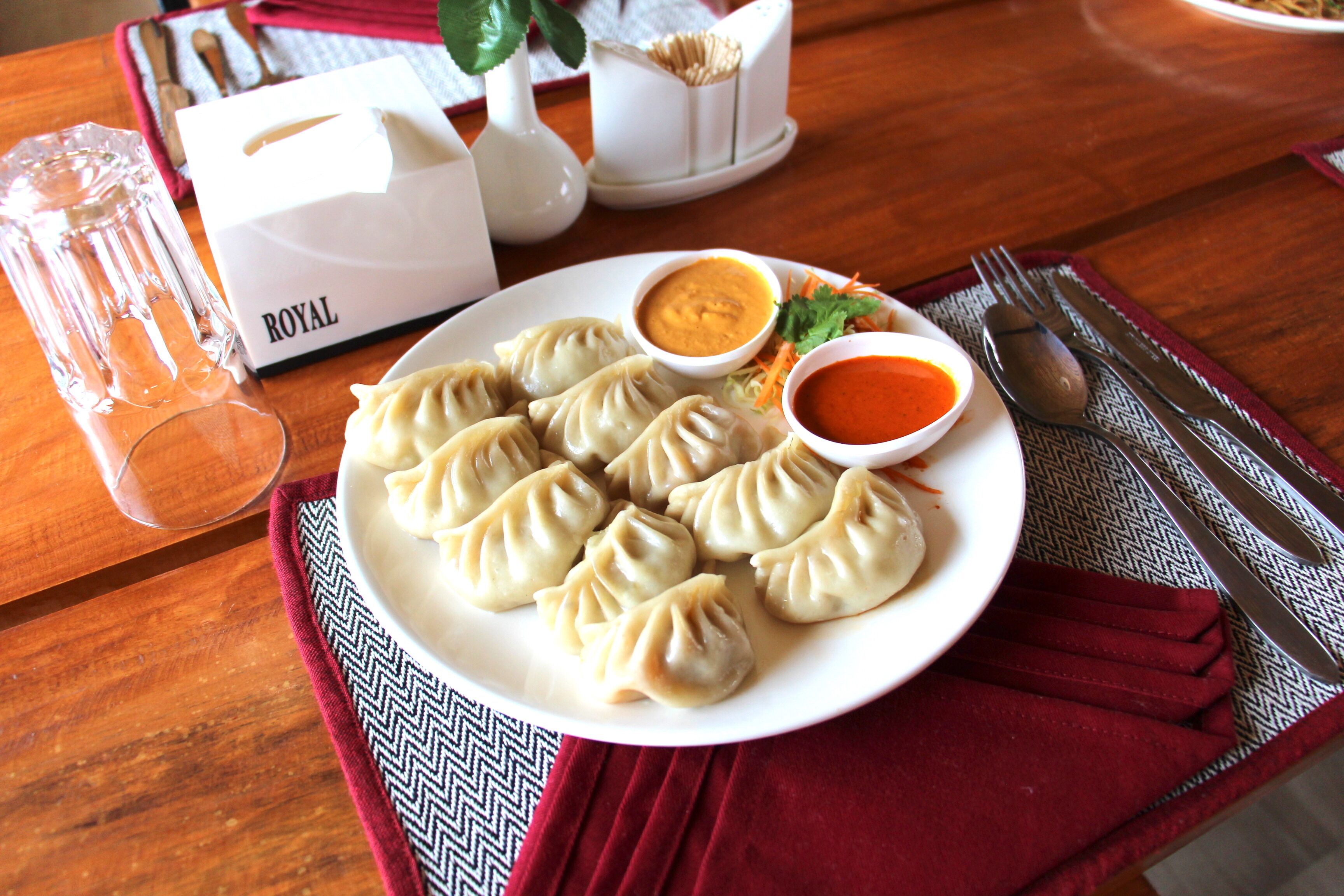 Un plat de dumplings amb salses per a acompanyar, un got d'aigua i una tovalla sobre una taula.