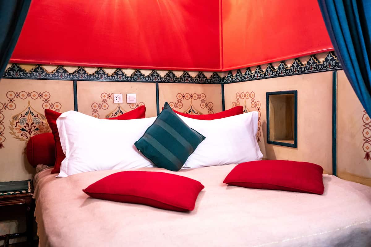 A bed with red and white pillows, a green striped pillow, and a red canopy.