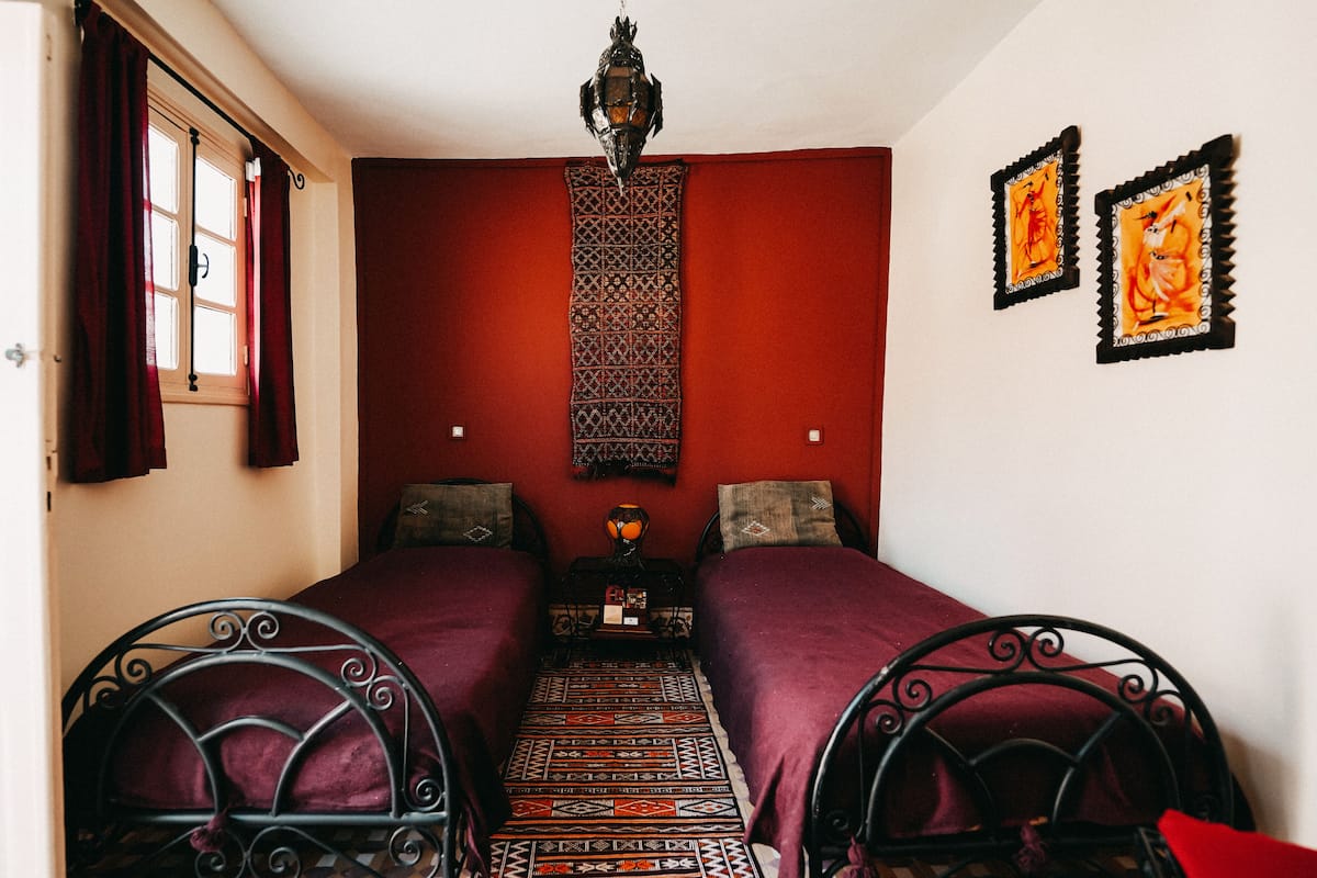 A room with two beds, a patterned rug, a hanging lantern, and two wall-mounted pictures.