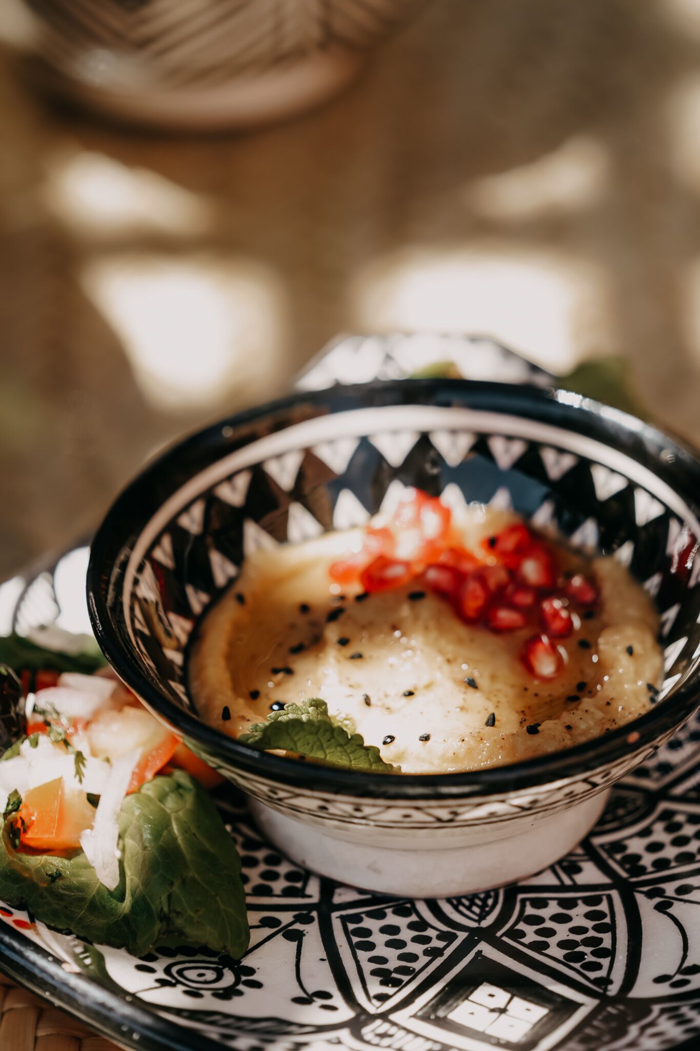 A bowl of food with pomegranate seeds on a patterned plate.
