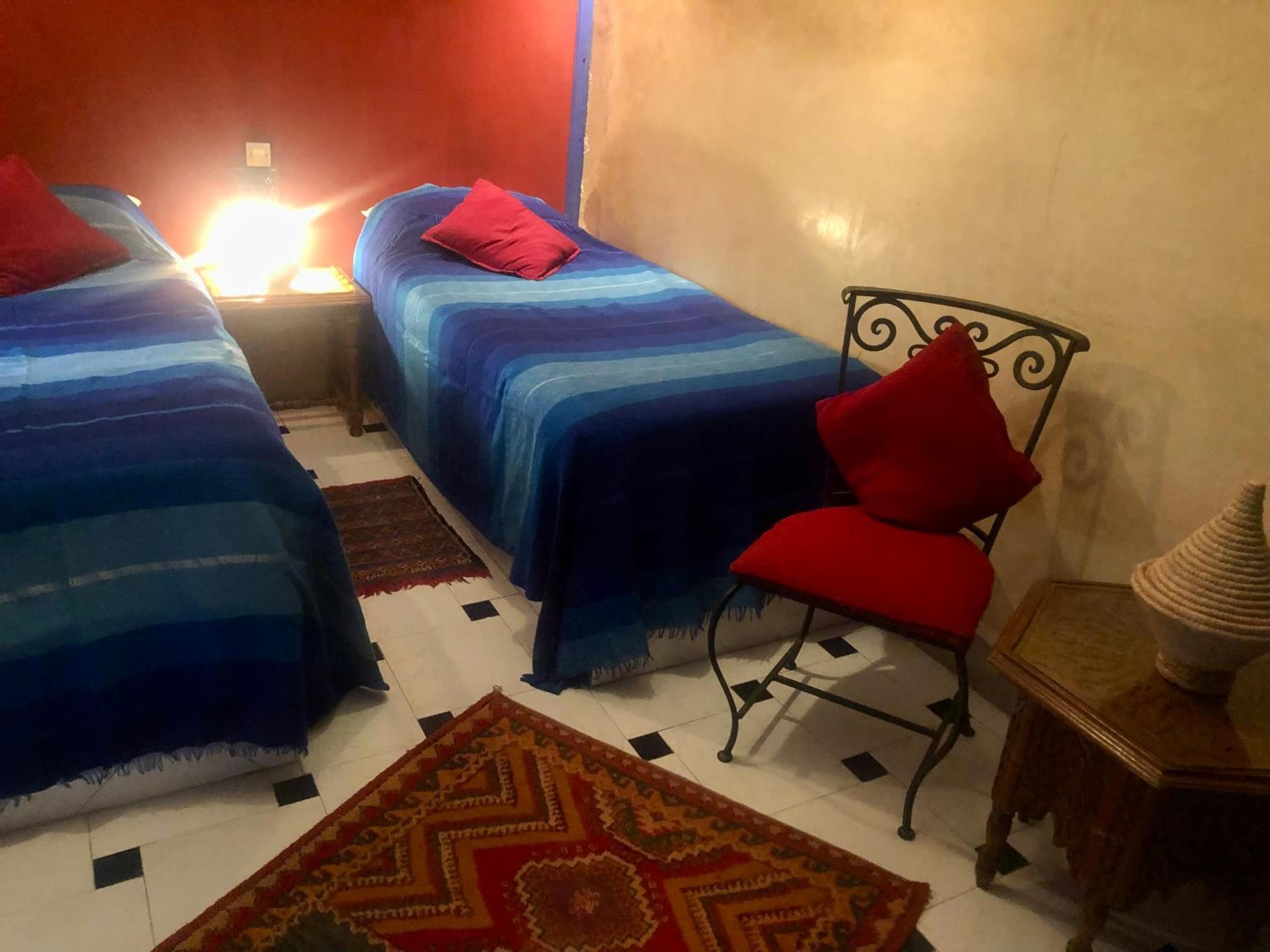 Una habitación con dos camas, una silla, una mesita pequeña y una alfombra.