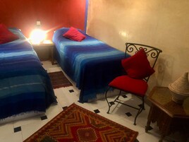 Una habitación con dos camas, una silla, una mesita pequeña y una alfombra.