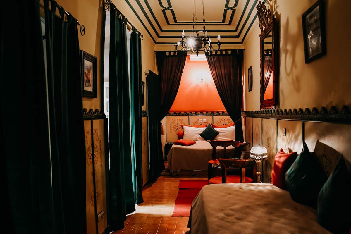 A hotel room with a bed, a nightstand, a lamp, and a view of the hallway.