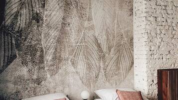A modern hotel room with two beds, a textured wall, a wooden headboard, and a small bedside table with a lamp.