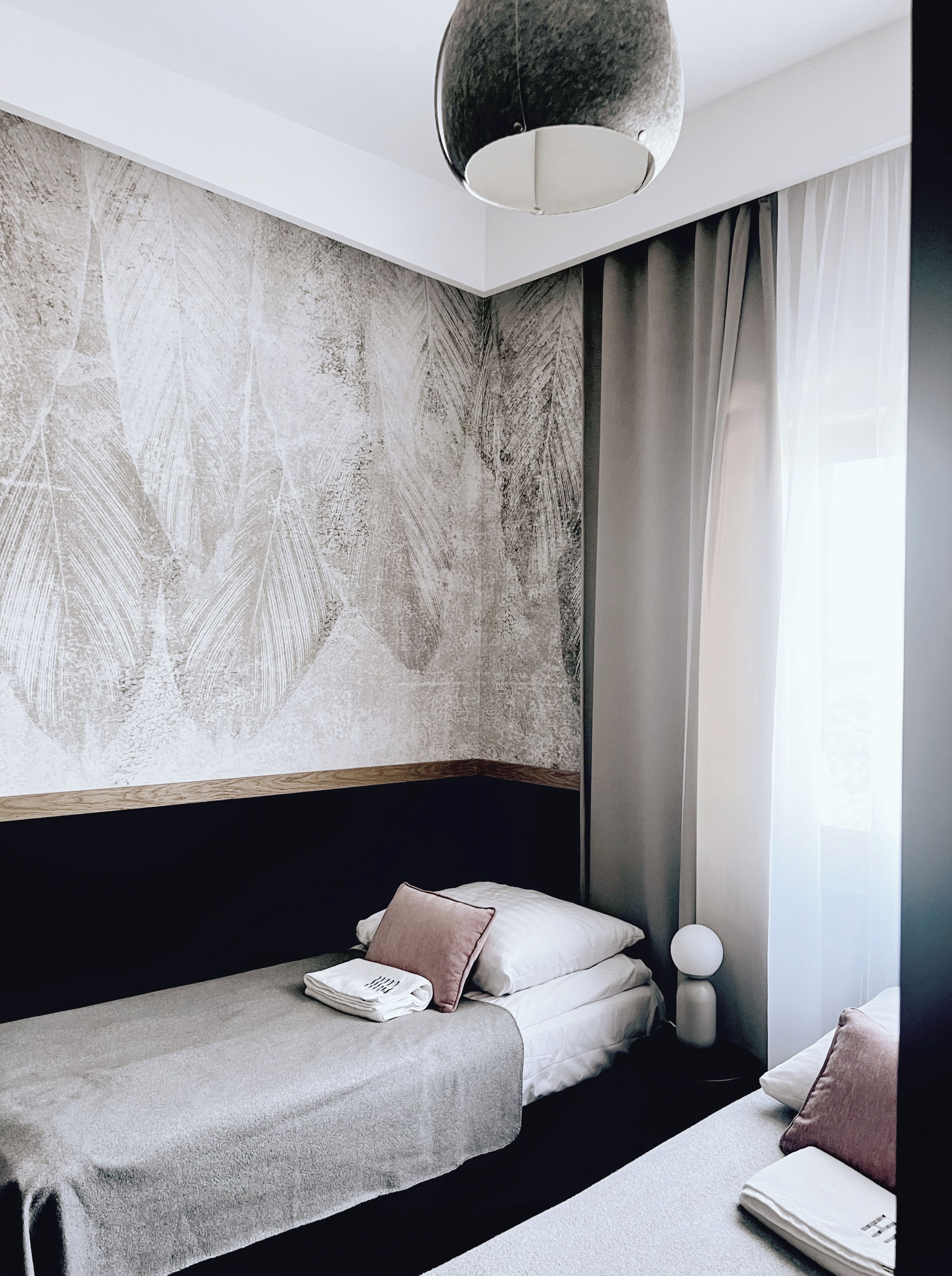 Ein modernes Hotelzimmer mit einer großen, strukturierten Wand, einem Bett mit Kopfteil, einem Nachttisch und einer Pendelleuchte.