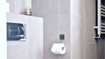 Et moderne badeværelse med hvidt toilet, grå flisevægge og trægulv.