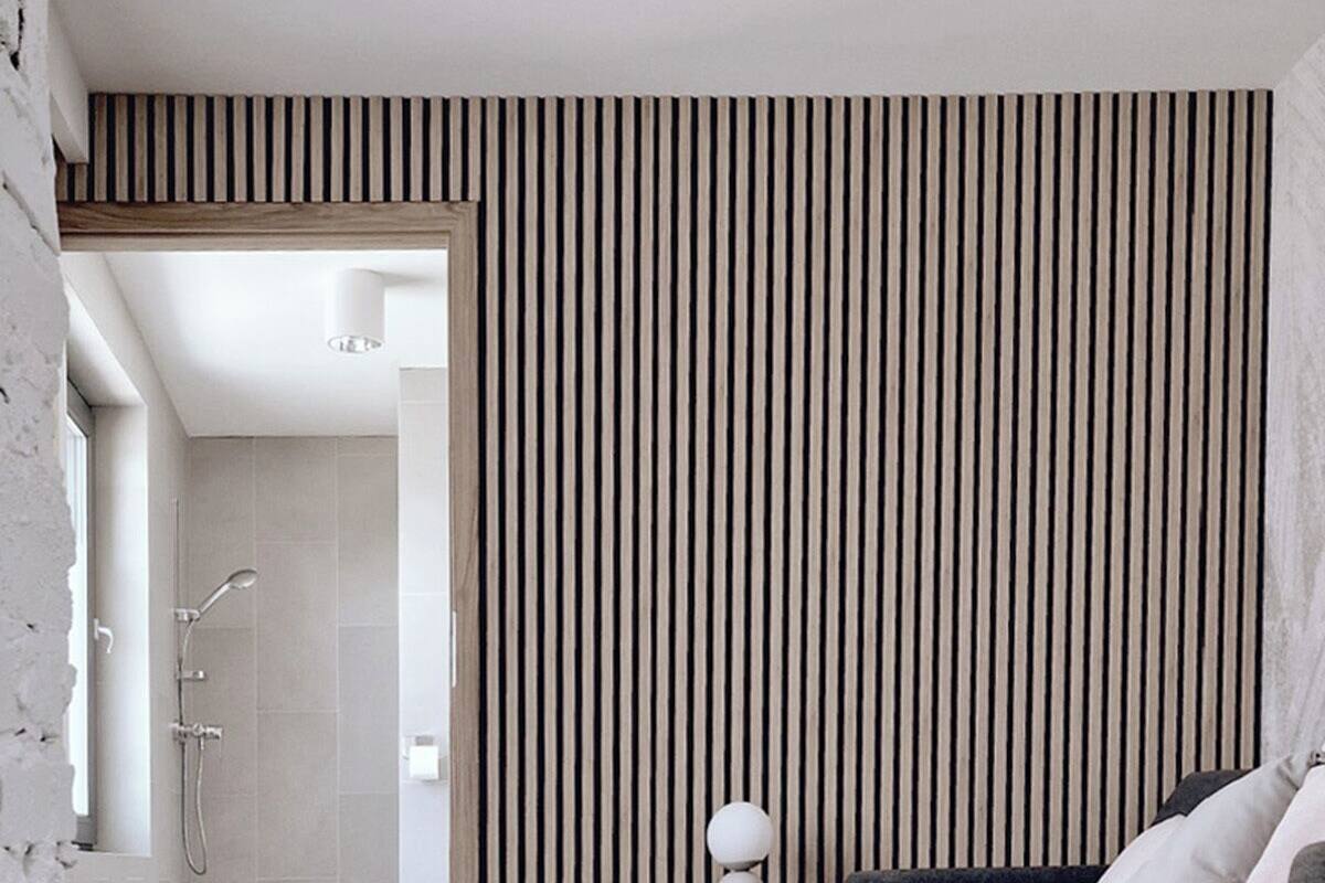 A modern hotel room with a grey sofa, a wooden slatted wall, and a visible shower area.