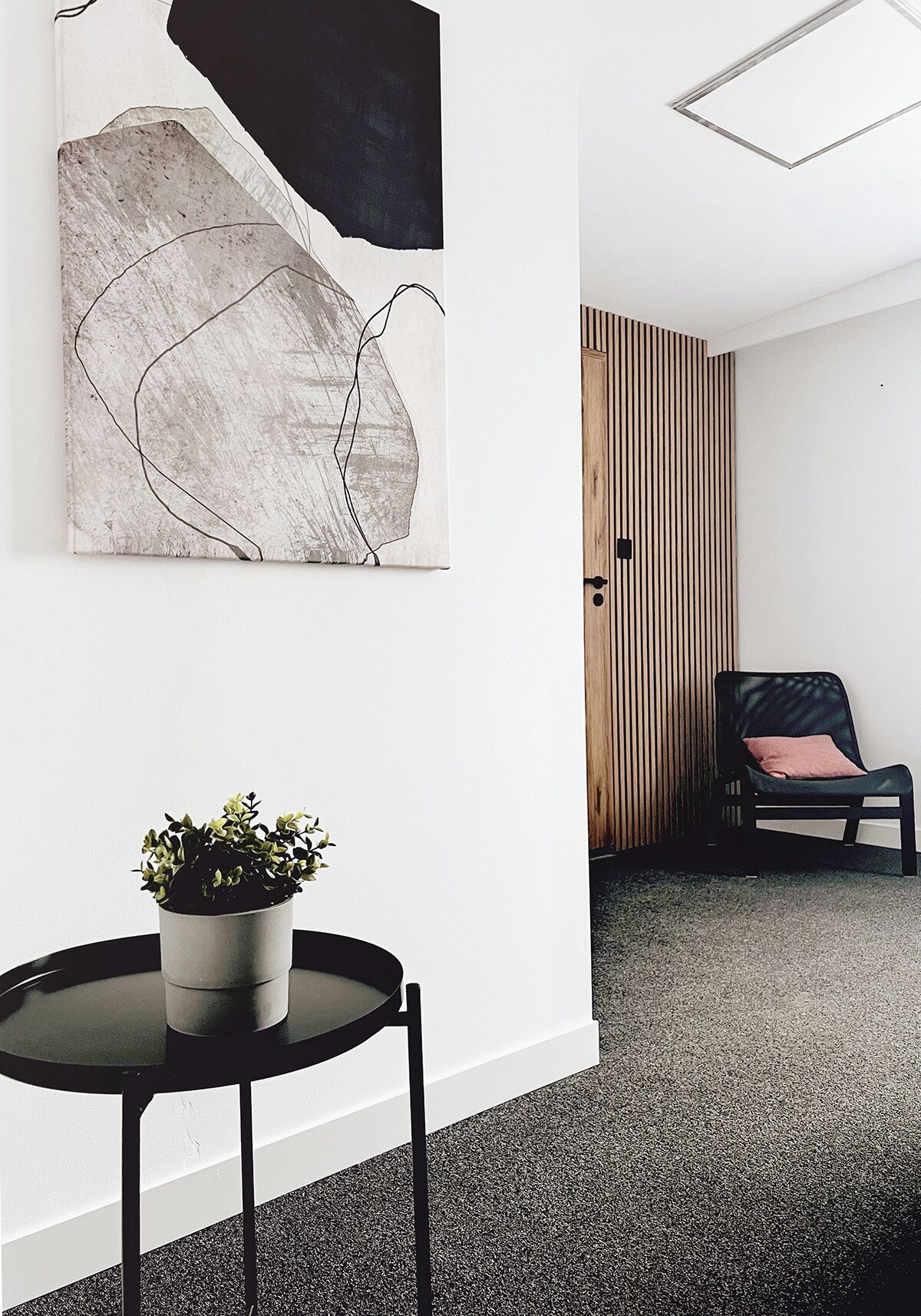A modern interior with a round table, a potted plant, a black chair, and a wooden slatted partition.