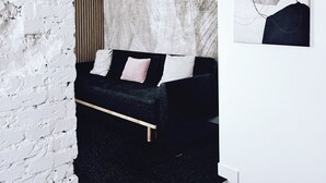 Un dormitorio moderno con un sofá negro, una pared de ladrillo blanco y un cuadro abstracto grande.