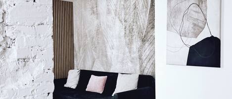 A modern bedroom with a black sofa, a white brick wall, and a large abstract painting.