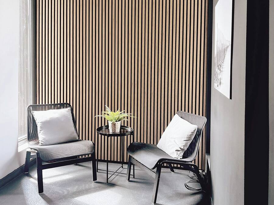 A modern room with two black chairs, a small round table with a plant, and a vertical striped wall.