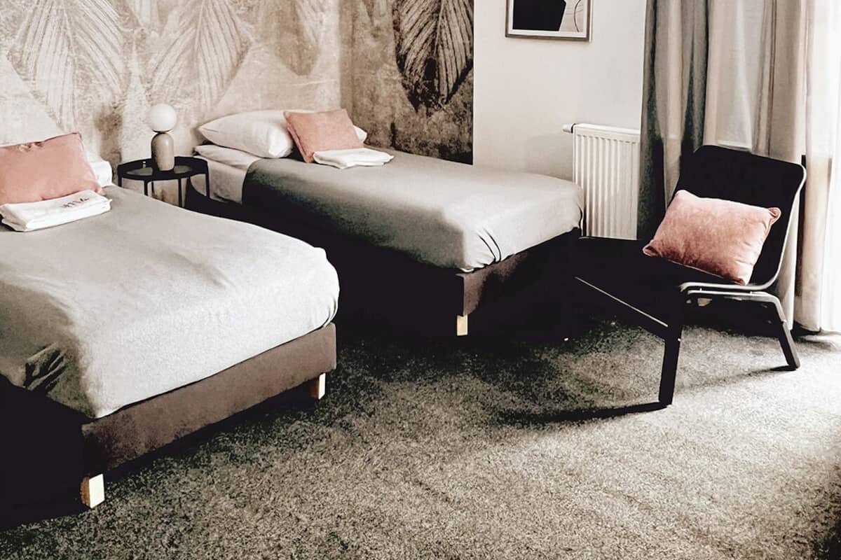 A modern hotel room with two beds, a chair, a radiator, and artwork on the walls.
