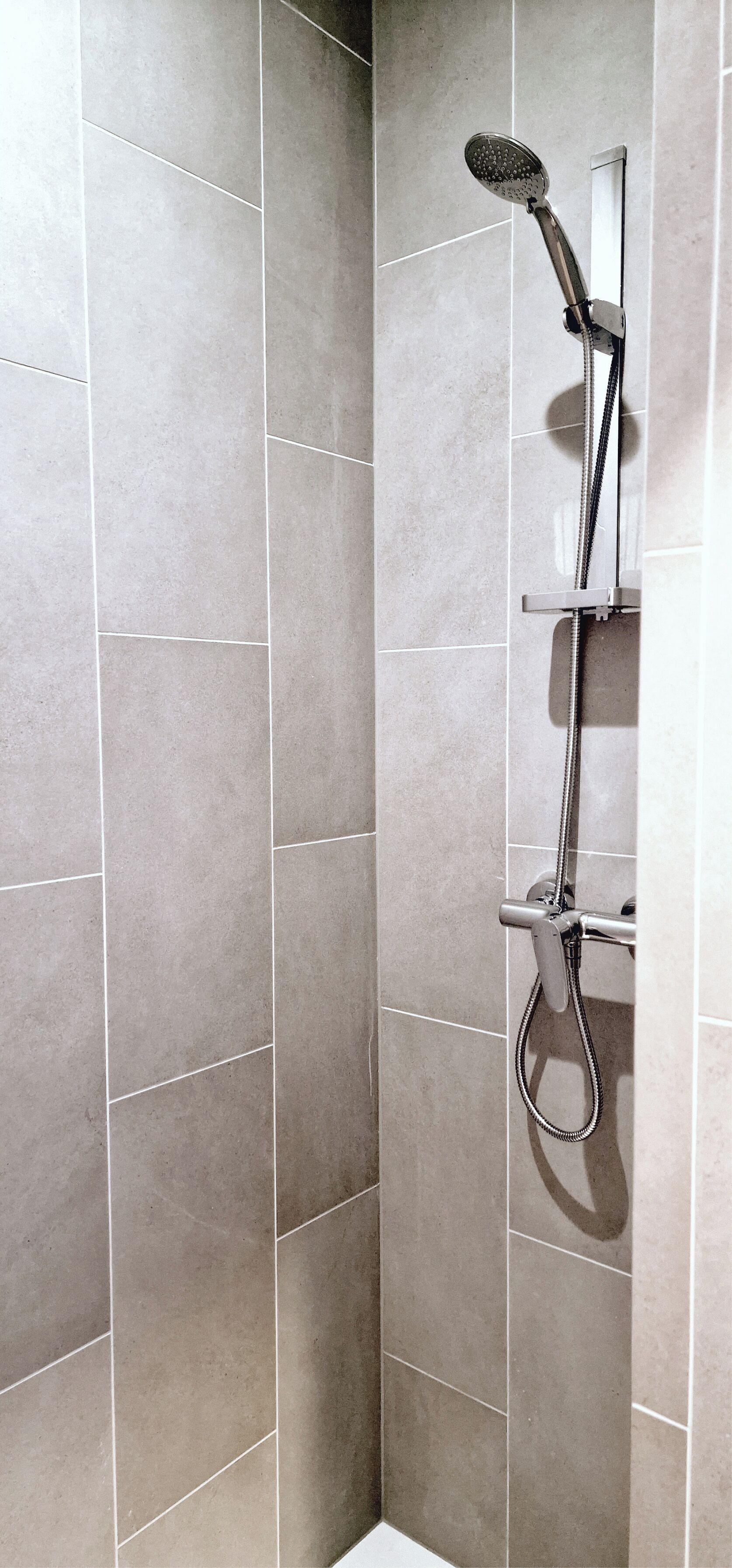 A shower with a handheld showerhead and a wall-mounted control panel.