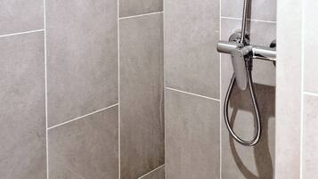 A shower with a handheld showerhead and a wall-mounted control panel.