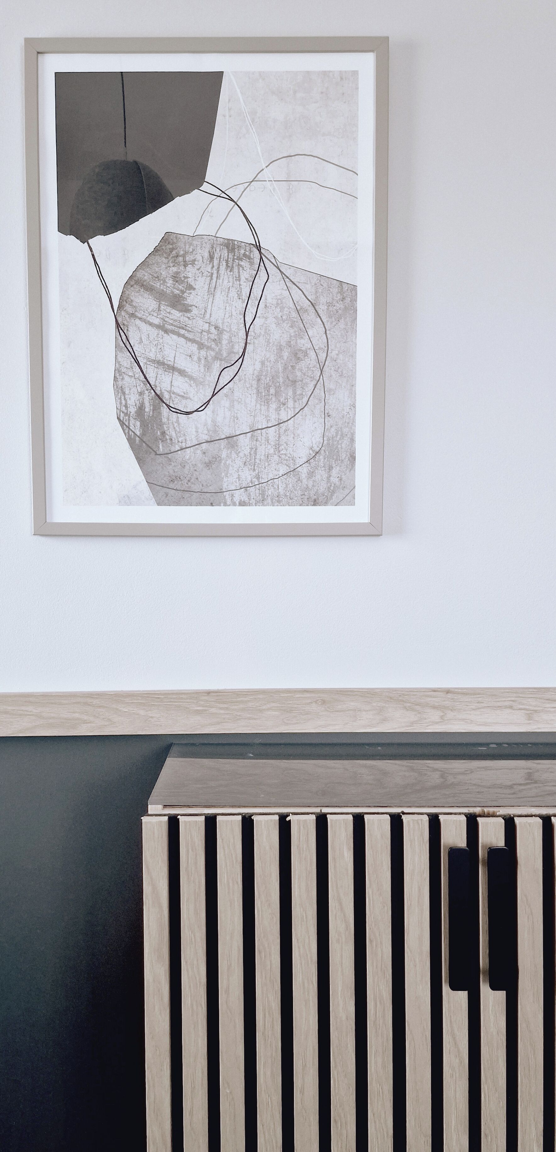 Una obra de arte abstracta enmarcadas en una pared sobre un mueble bajo de madera.
