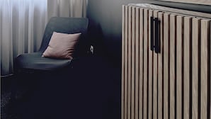 Habitación de hotel con una silla, un radiador y dos cuadros en la pared.