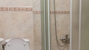 Un bany amb vàter, plat de dutxa amb porta de vidre i una tovallola groga a terra.