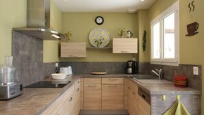 A modern kitchen with wooden cabinets, a stainless steel range hood, a coffee maker, and a window with a view.