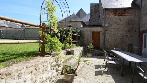 A courtyard with a pergola, potted plants, a stone wall, and a table with chairs.