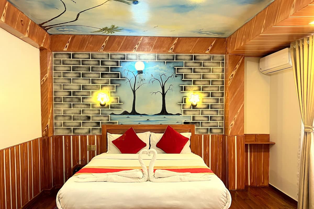 A hotel room with a brick-patterned wall, a bed with red pillows, and two wall-mounted lights.