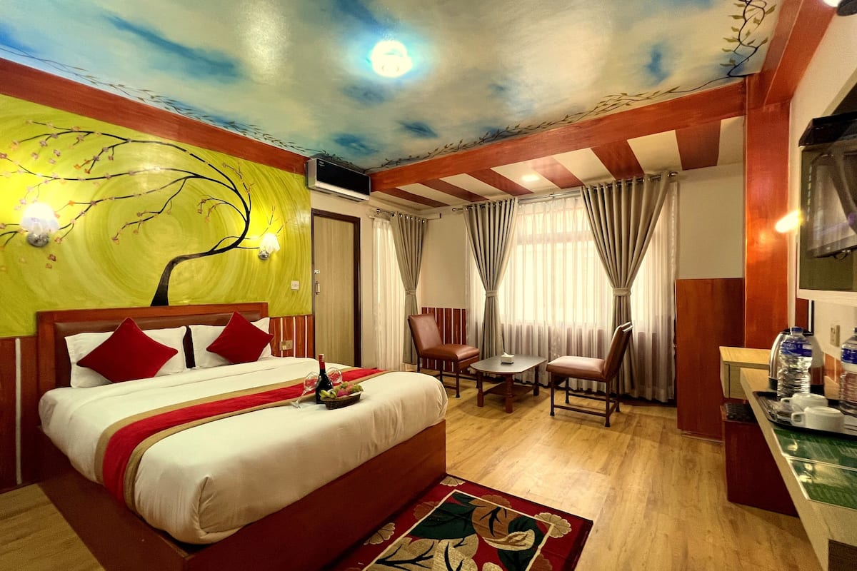 A hotel room with a bed, a small table, two chairs, a desk with a computer, and a window with curtains.