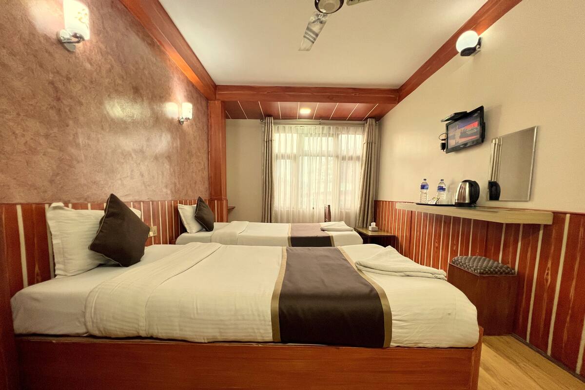 A hotel room with two beds, wooden paneling, a ceiling fan, a television, and a small table with a mirror and toiletries.