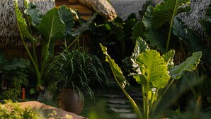 A garden with thatched-roof structures, lush greenery, and a large potted plant. - JoyStay - Hostel (Hai Phong)