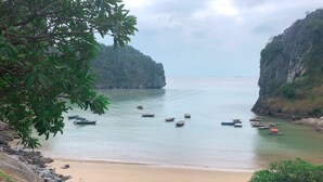 A coastal scene with boats on calm waters, a sandy beach, and rocky cliffs. - JoyStay - Hostel (Hai Phong)