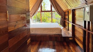 A bedroom with a sloped ceiling, wooden walls, a large window, and a bed. - JoyStay - Hostel (Hai Phong)