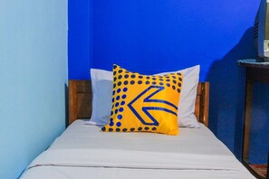 Un lit avec un matelas blanc et un seul oreiller orné d’un motif géométrique.
