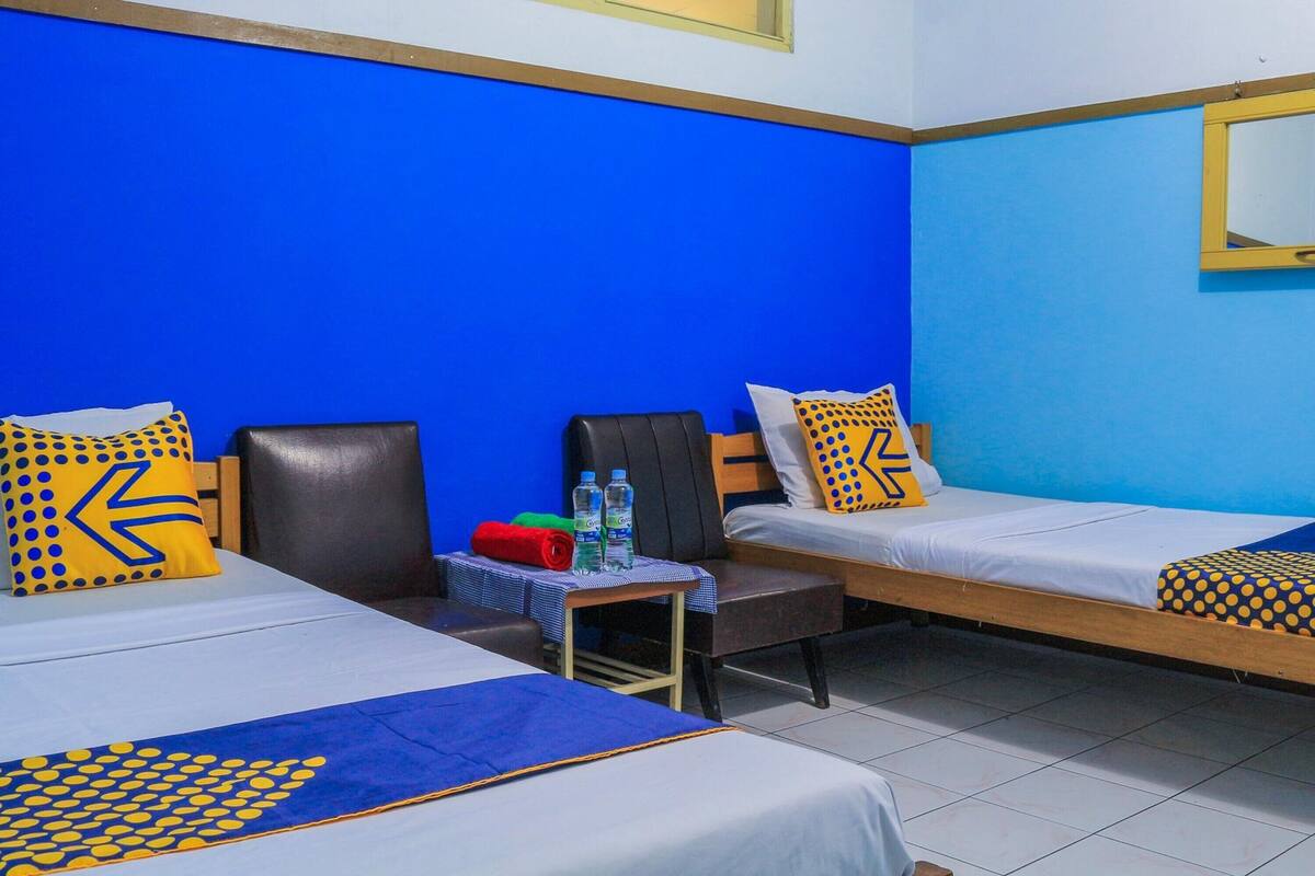 Una habitación de hotel con dos camas individuales, una mesita con botellas de agua y una silla.